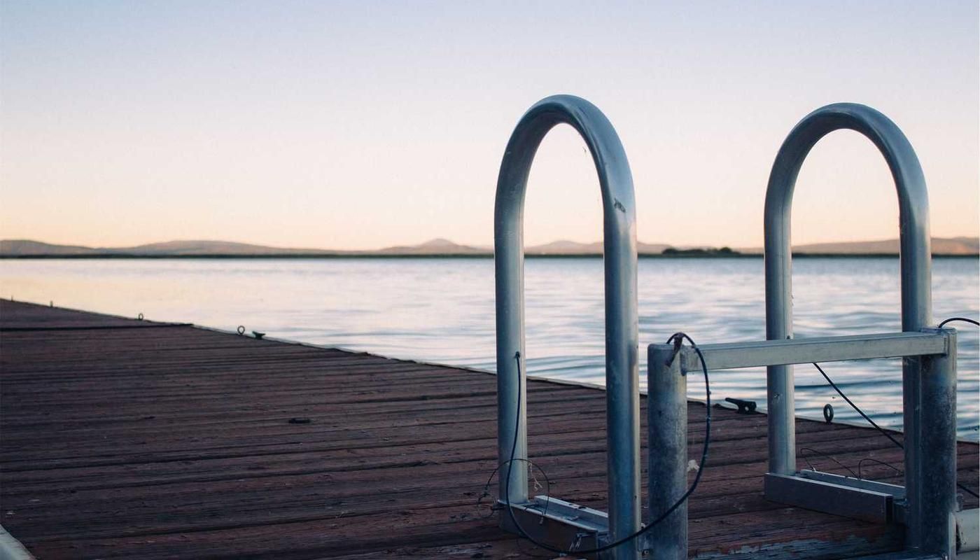Metal dock ladder extending over calm waters at dusk, part of a wooden pier in Panama City, ideal for cultural tours to Embera Village