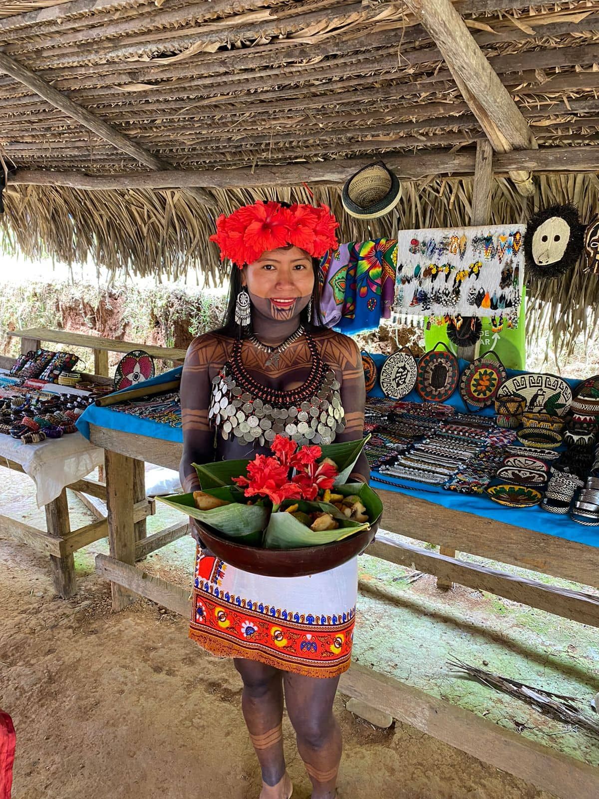 Embera indigenous woman in traditional attire holding a bowl of food at a cultural market in Panama.