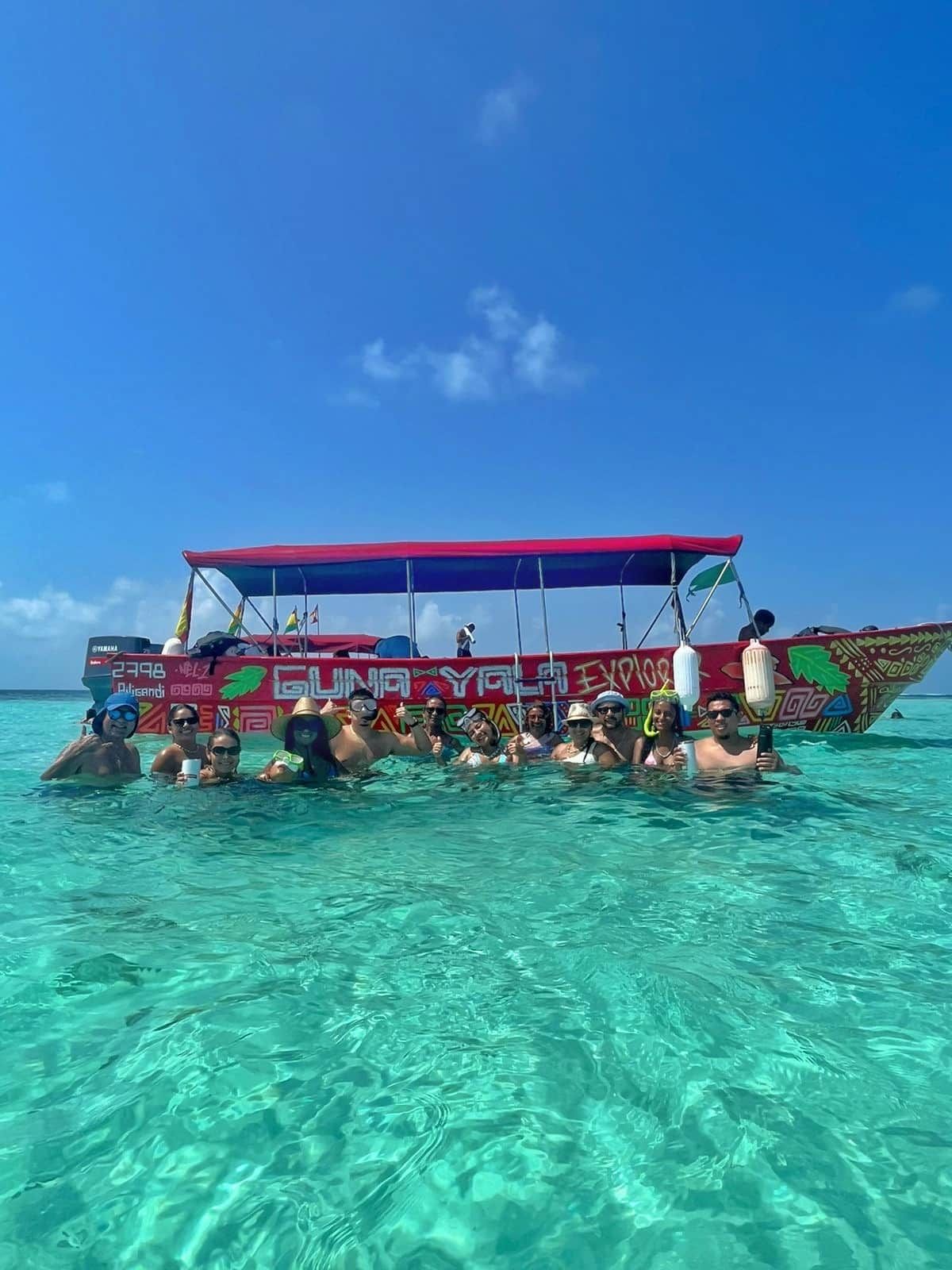 Group of people swimming near a colorful 'Guna Yala Explore' boat in the turquoise waters of the San Blas Islands during a sunny day tour in Panama.