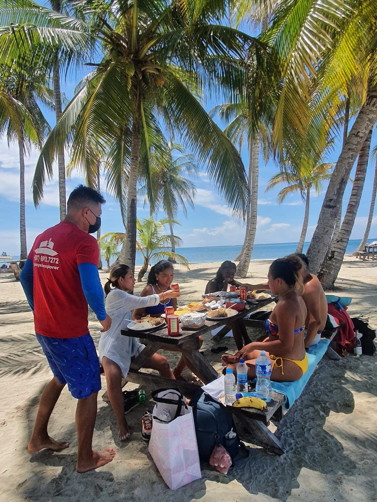 Group of people enjoying a beach picnic under palm trees during the San Blas Islands Day Tour Guna Yala in Panama City, Panama.