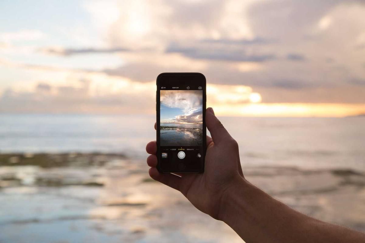 A hand holding a smartphone captures a stunning sunset over the ocean at Pipeline Road, Panama City, Panama.