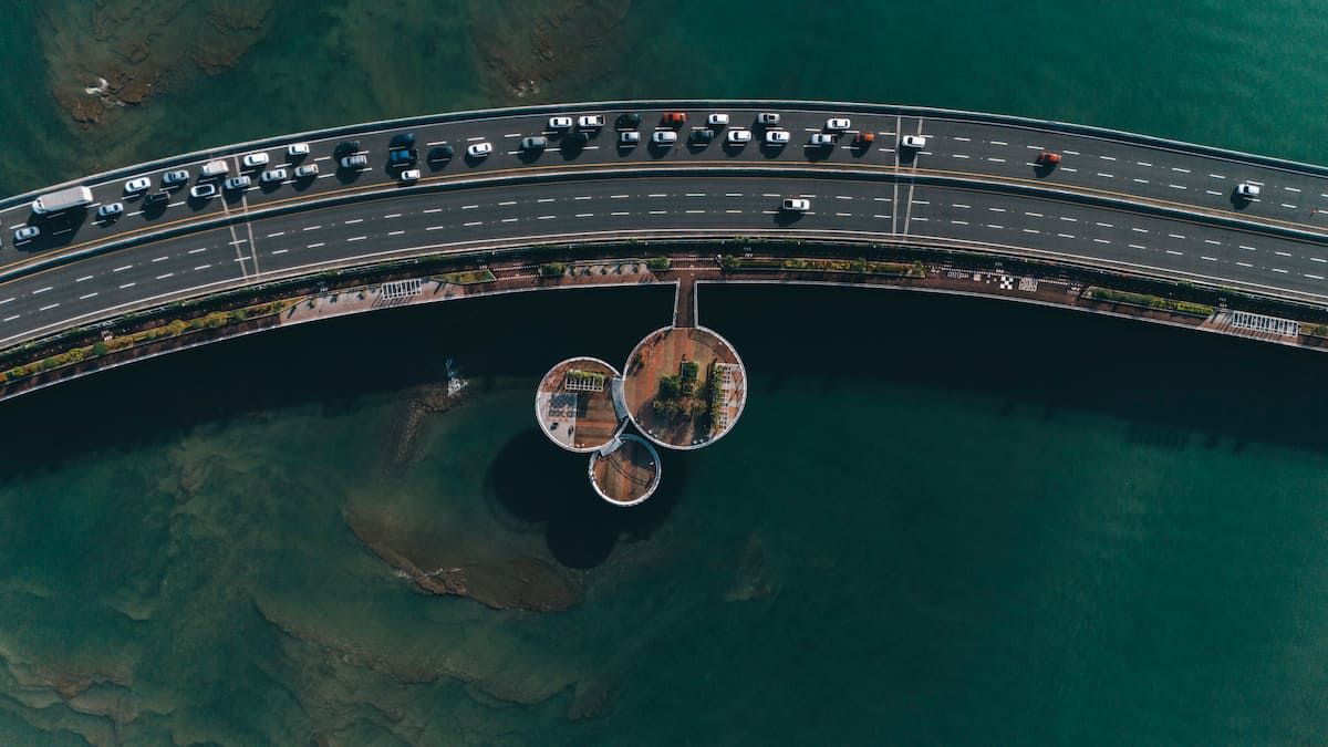 Aerial view of a curved bridge over turquoise waters with vehicles and circular structures beneath, showcasing modern infrastructure in Panama City.