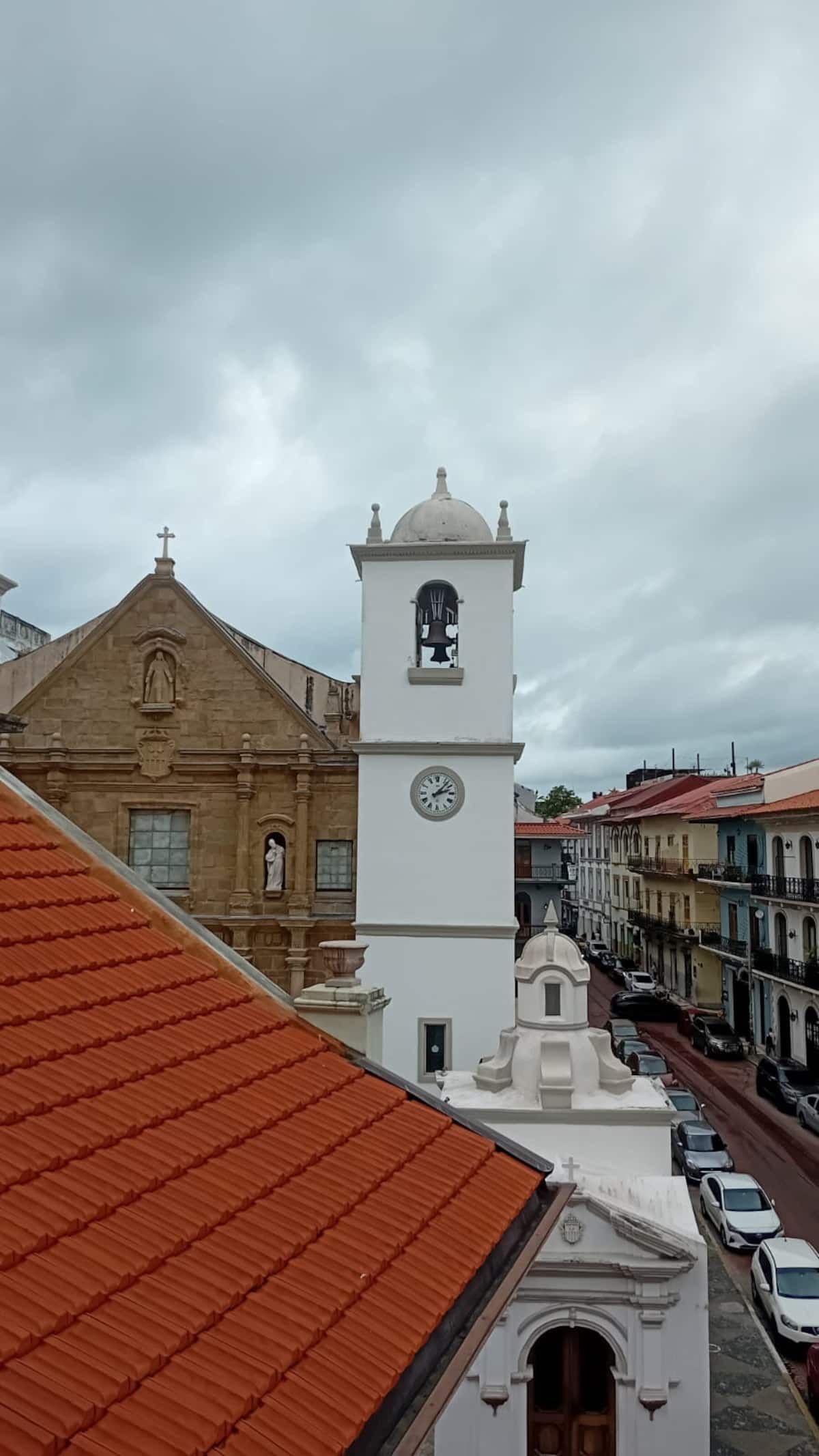 White clock tower with bell and historic church in Old Town Casco Viejo, Panama City, under an overcast sky.