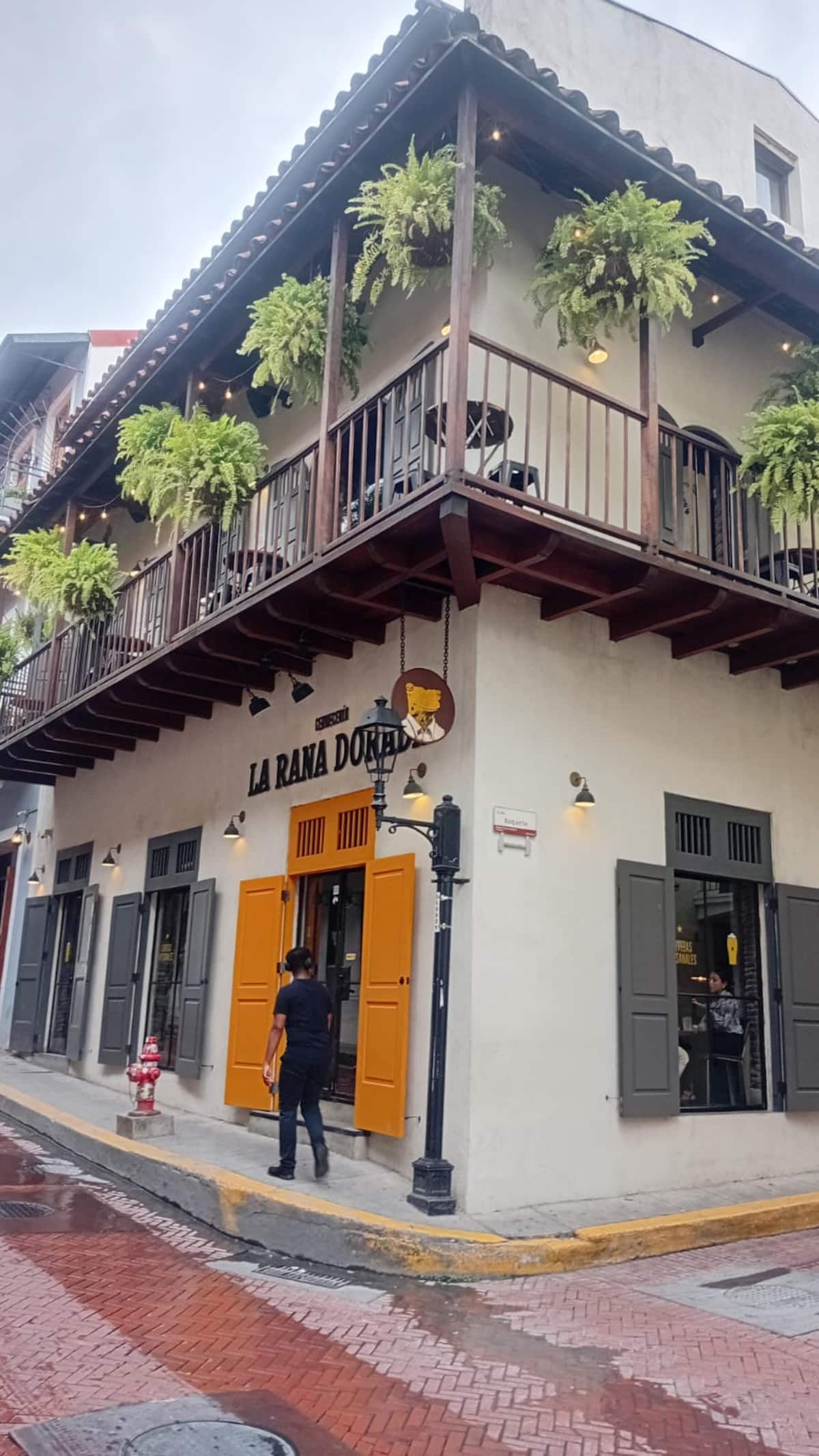 Exploring Old Town Casco Viejo: La Rana Dorada restaurant with its iconic orange shutters and balcony adorned with ferns, set against the backdrop of historic Panama City streets.