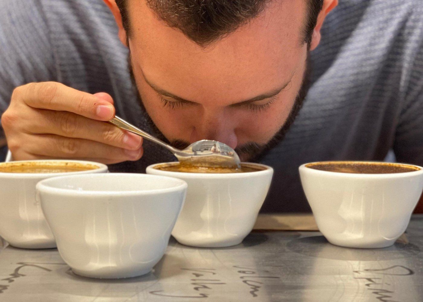 A man carefully tasting Geisha coffee during a chocolate-infused coffee experience in Panama City, surrounded by four white cups of coffee on a metal table.