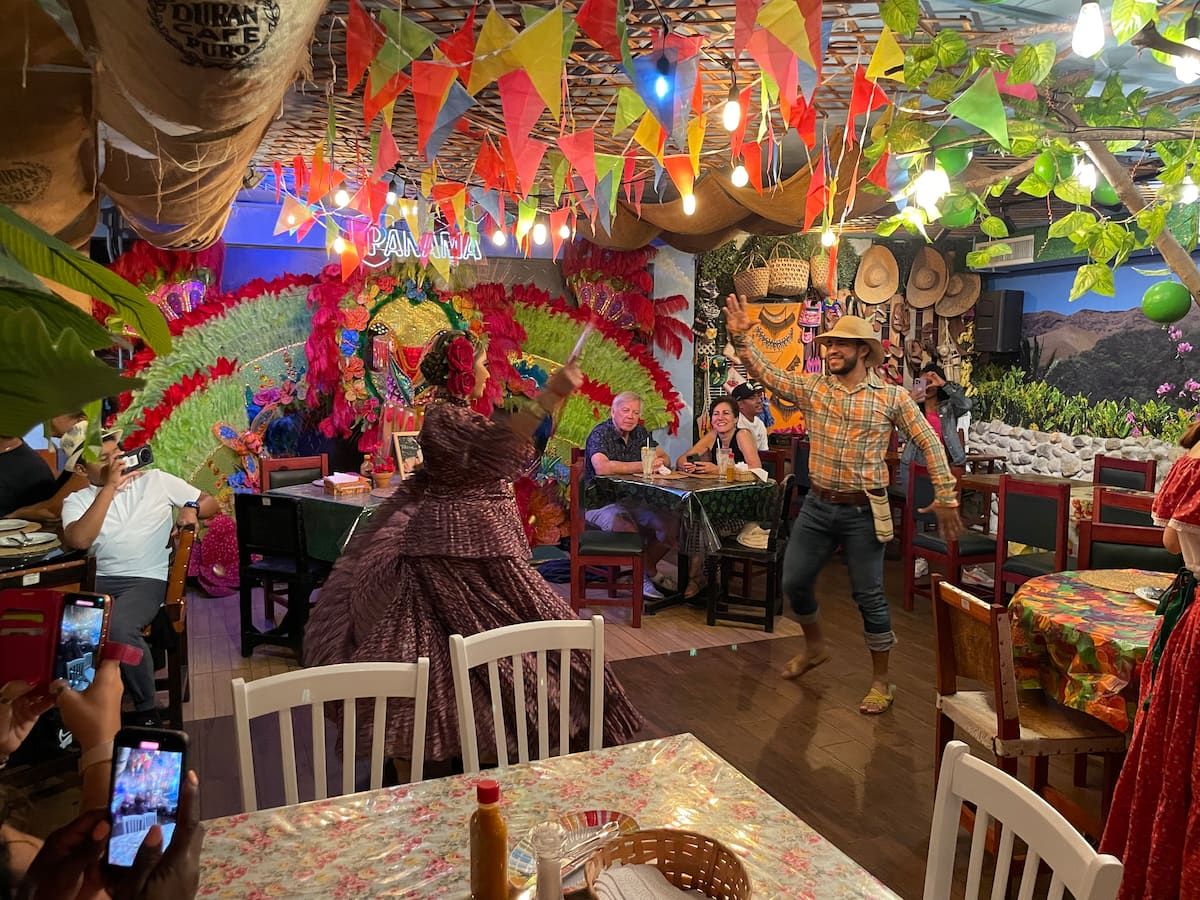 Guna cultural dancers perform in a festively decorated restaurant during the Urban Tour in Casco Viejo, Panama City, with diners capturing the lively scene on their phones.