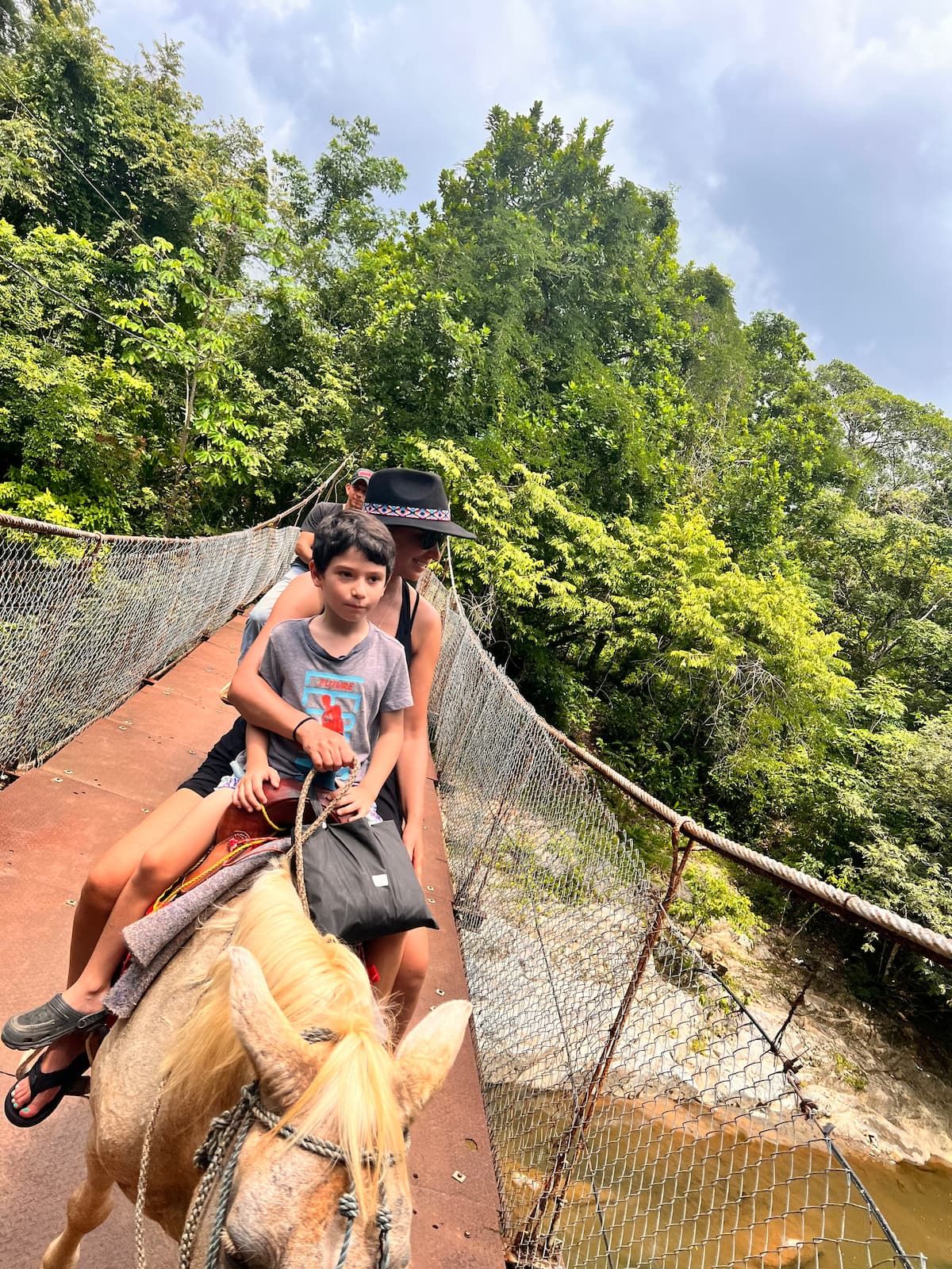 Woman and child riding a horse on a suspension bridge amidst lush green forest in Panama City, Panama