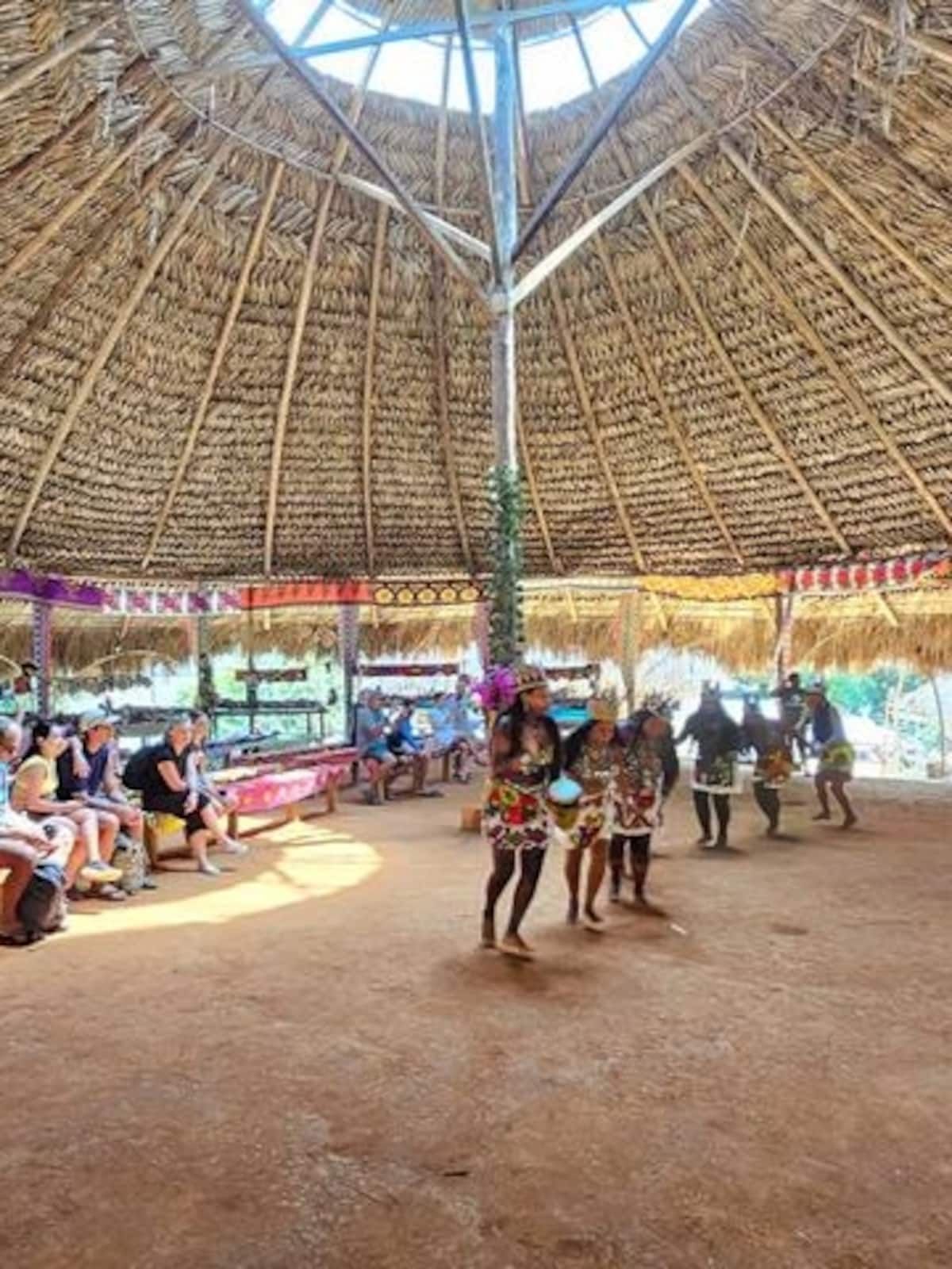 Embera dancers in traditional attire perform a cultural dance inside a thatched hut for tourists at an Indigenous village in Panama
