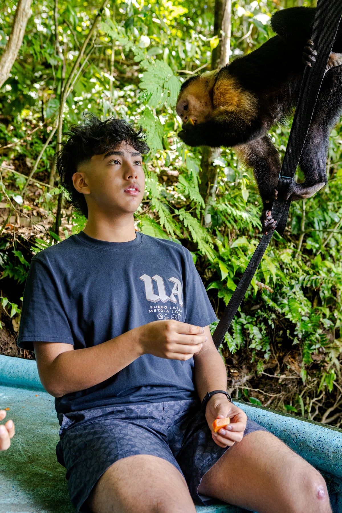 Young man feeding a capuchin monkey during a tour at Gatun Lake, Panama City, surrounded by lush green jungle foliage.