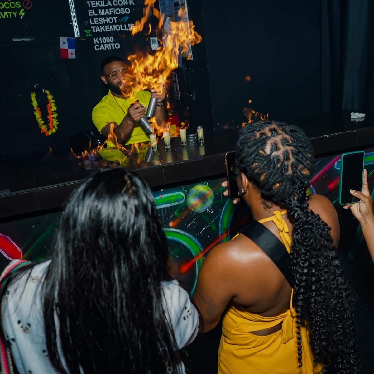 Bartender performing a flaming drink preparation at a vibrant bar during a Panama Bar Crawl in Casco Viejo, captured by onlookers.