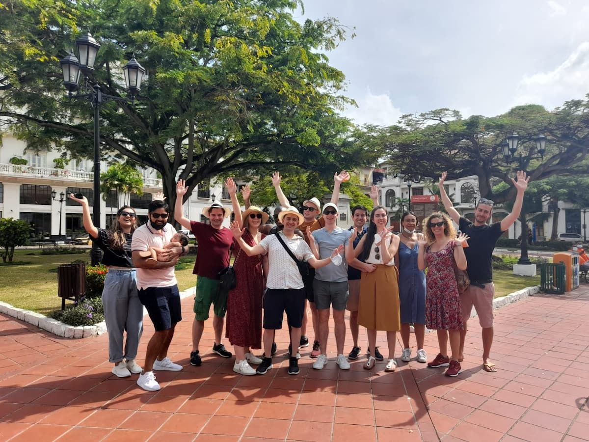 Group of tourists waving during the Panama Canal Locks Casco Viejo Tour in Panama City, Panama, captured on a sunny afternoon with colonial architecture and lush greenery in the background.