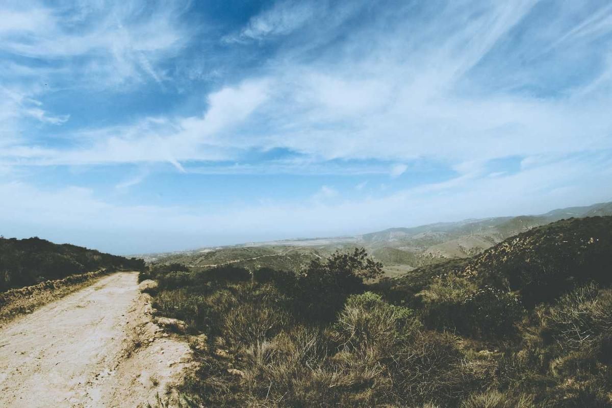 A winding dirt road through rolling hills under a blue sky with wispy clouds, showcasing the natural beauty of Panama City's countryside.