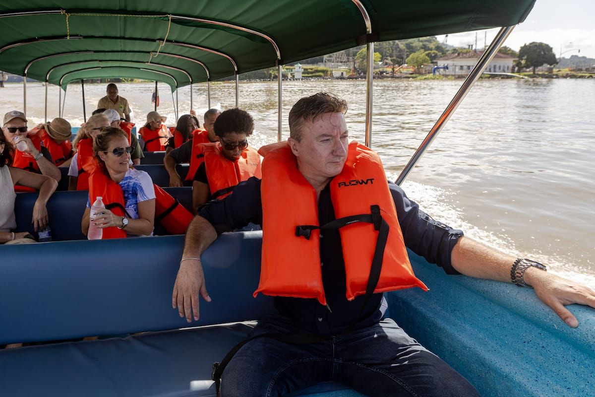 Tourists wearing orange life jackets enjoy a boat ride on the Panama Canal with Monkey Island in the background.