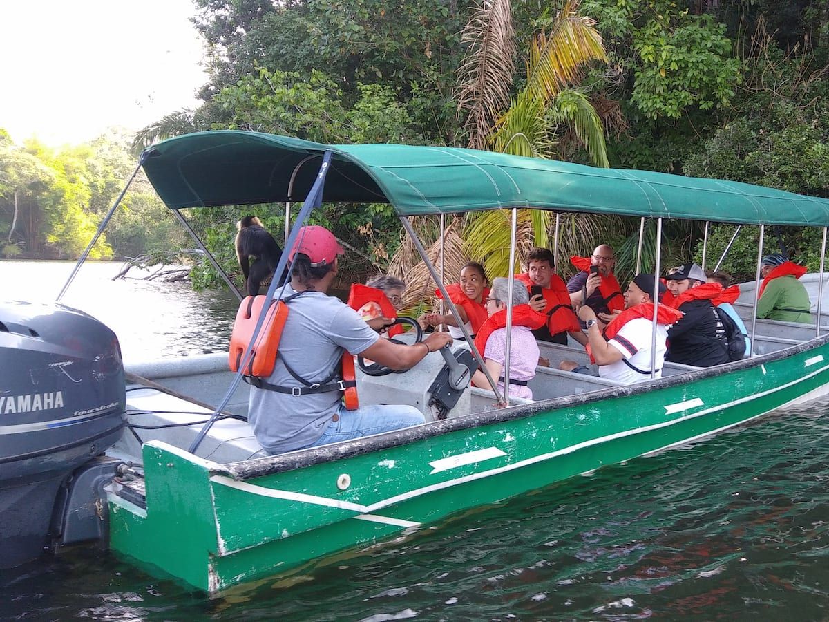 Tourists enjoying a boat ride with a monkey on the Panama Canal Monkey Island Tour, surrounded by lush jungle scenery.
