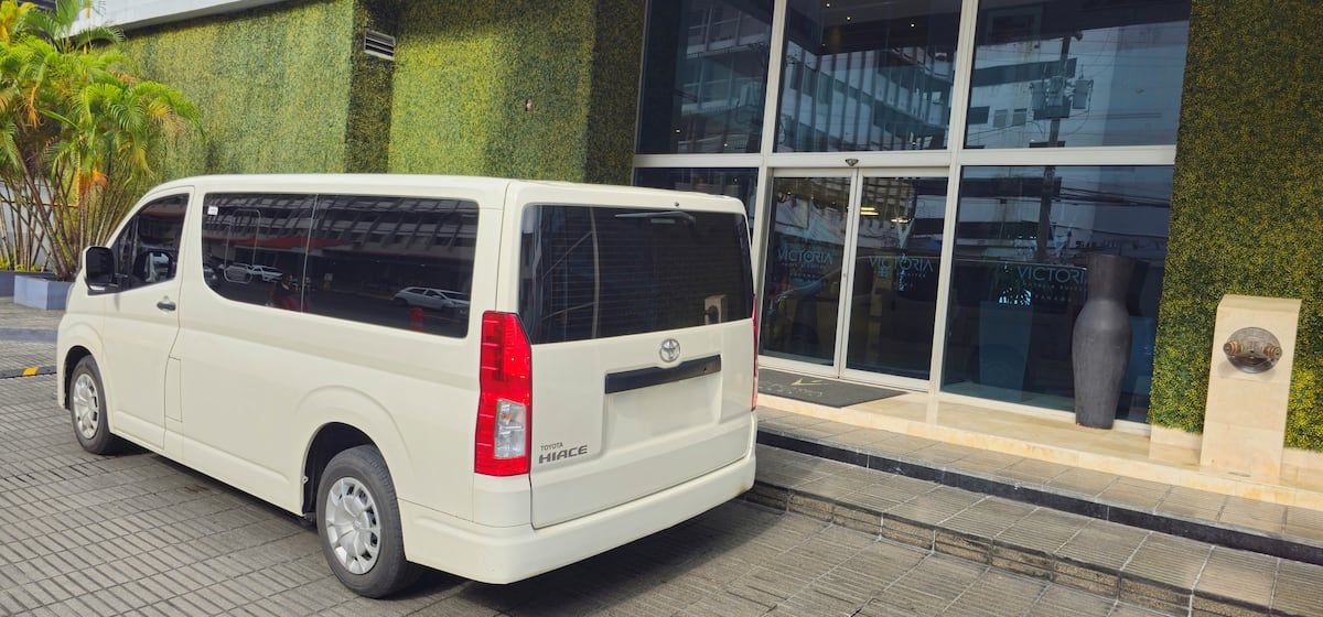 White Toyota Hiace van parked outside a modern building entrance in Panama City, part of Bandits Adventure Tours Panama's transportation for the Panama Canal Monkey Island Tour.