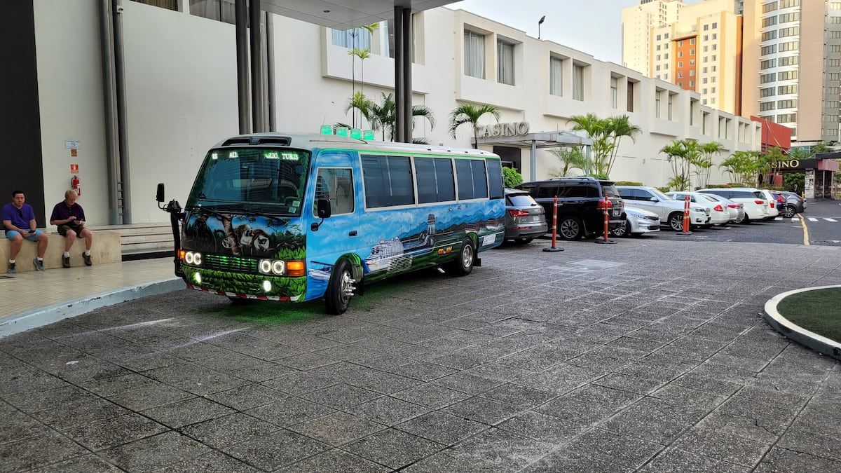 Colorful shuttle bus painted with tropical artwork parked outside a casino in Panama City, with tourists waiting nearby for the Panama Canal Tour Miraflores Locks City Highlights.