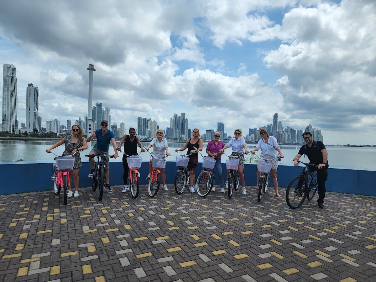 Group of tourists on bicycles during a Panama City Bike Tour, capturing skyline views and photo stops in Casco Viejo against a backdrop of modern skyscrapers and a partly cloudy sky.