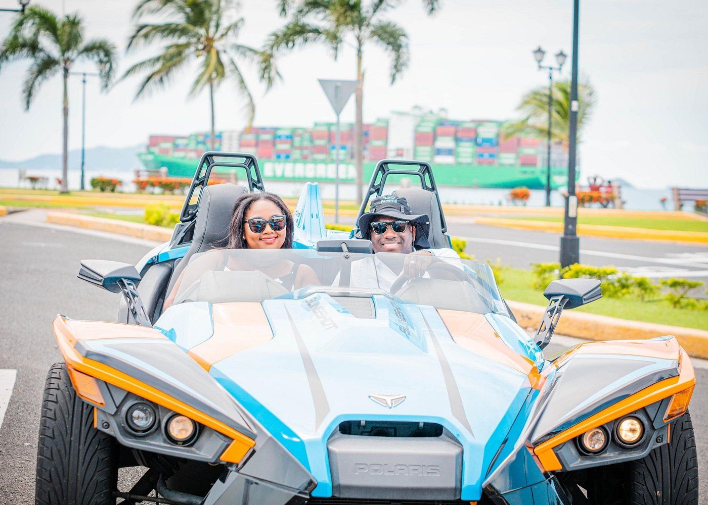 Couple enjoying a sightseeing tour in a Polaris Slingshot on the Amador Causeway in Panama City, with a cargo ship in the background.