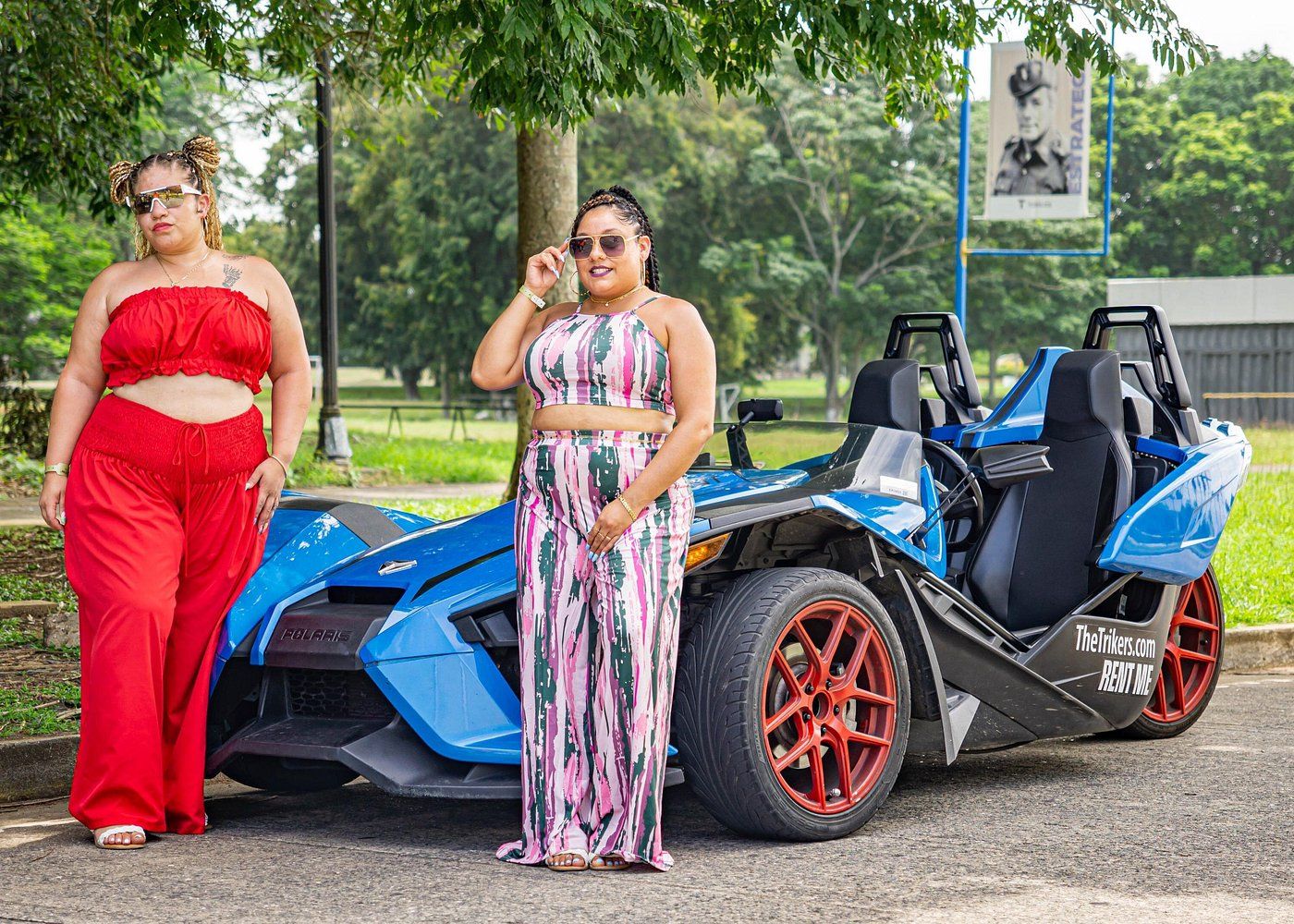 Two women in colorful outfits posing next to a blue Polaris Slingshot during a sightseeing tour in Panama City, Panama.