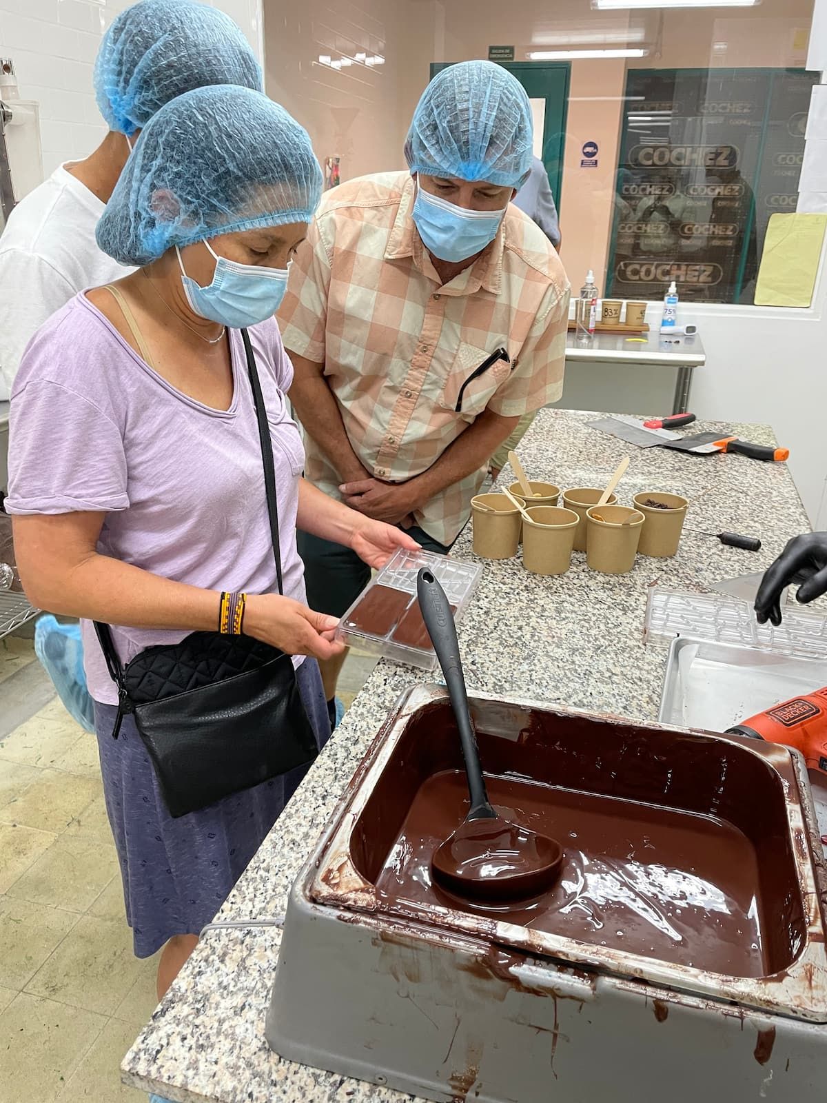 Tourists wearing hairnets and masks examine chocolate molds during a Panamanian Chocolate Bean To Bar Tasting workshop in Panama City.