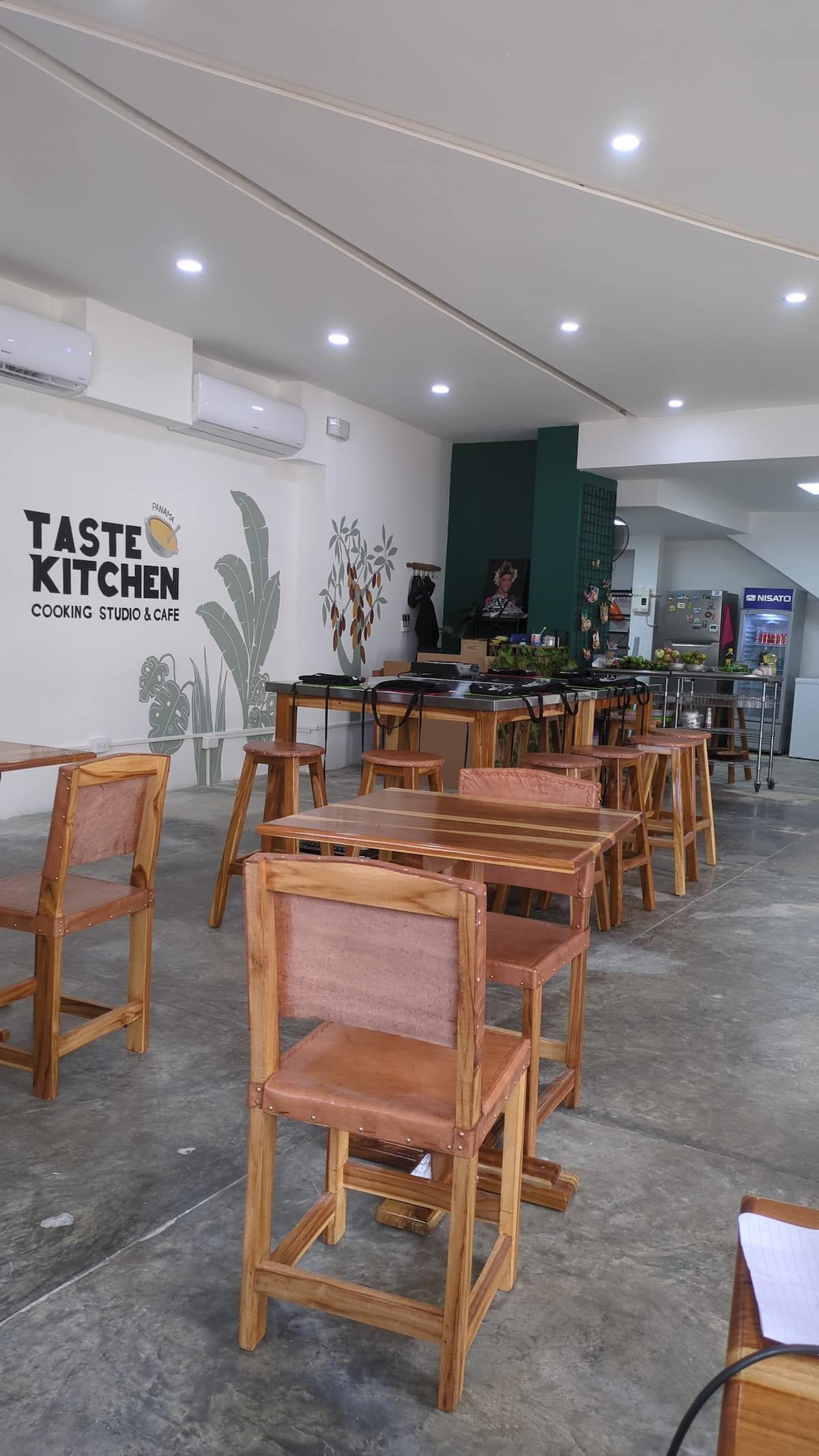 Interior of Taste Kitchen Cooking Studio & Café in Casco Viejo, Panama City, featuring wooden tables, chairs, and a cooking station with fresh ingredients.