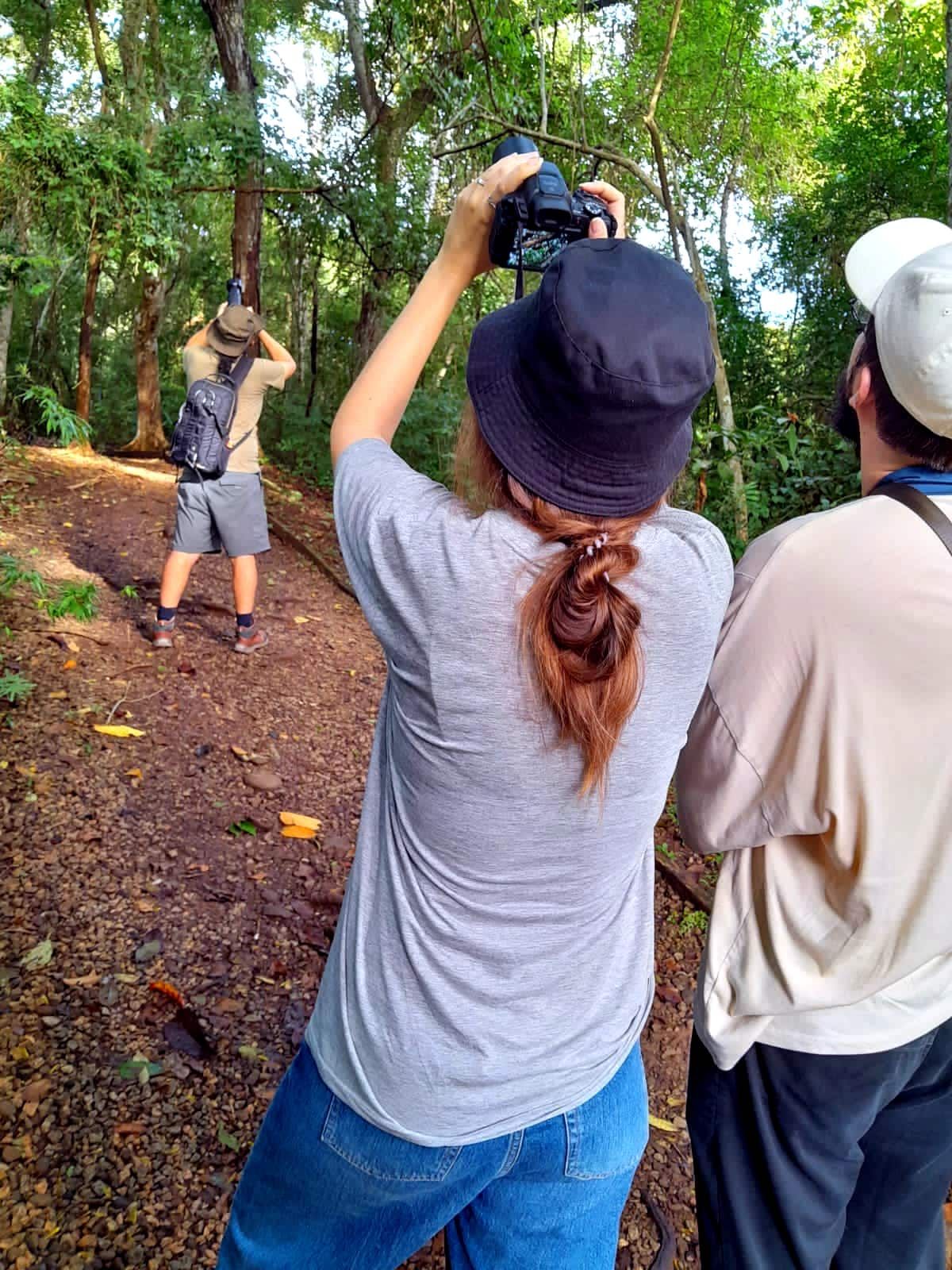Woman taking a photo with a DSLR camera during a photowalk in the Panama Rainforest Metropolitan Park, surrounded by lush greenery and fellow participants.
