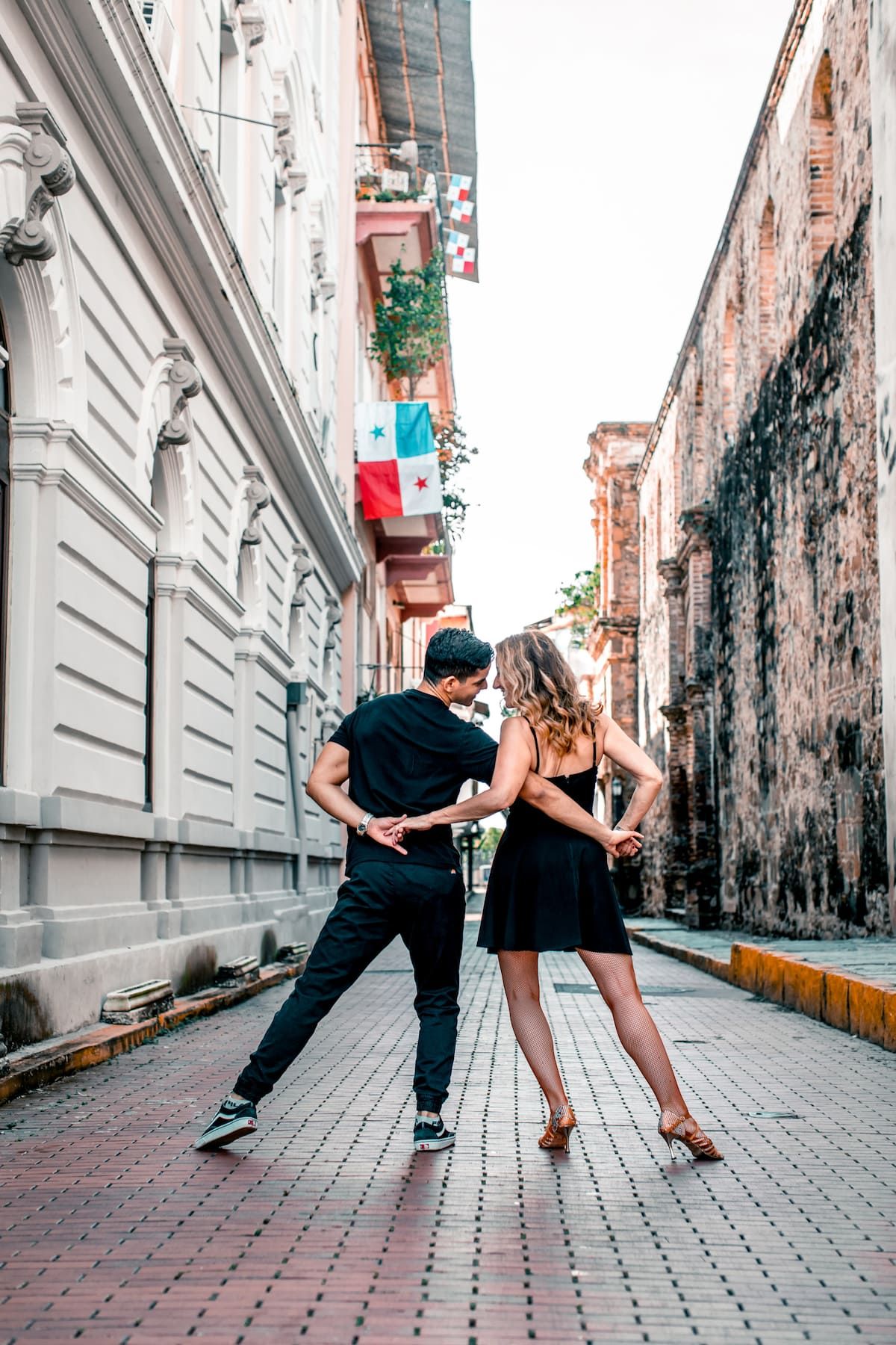 Couple dancing salsa on a cobblestone street in Panama City, surrounded by colonial architecture and a waving Panama flag.