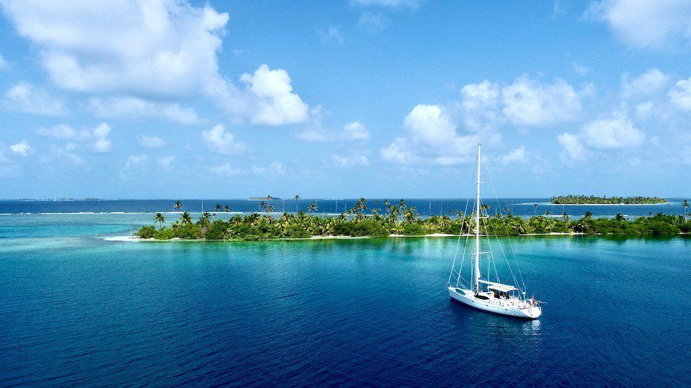 A sailboat glides across turquoise waters near a lush tropical island under a bright blue sky during a San Blas Islands day trip from Panama City