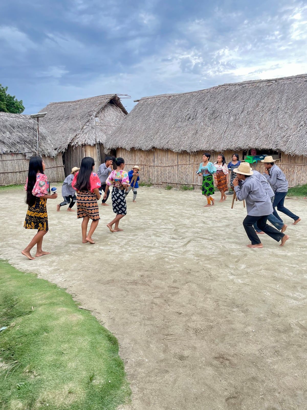 Group of people performing a traditional dance in a rural village setting with thatched-roof huts in the background during a San Blas Islands Day Trip in Panama.