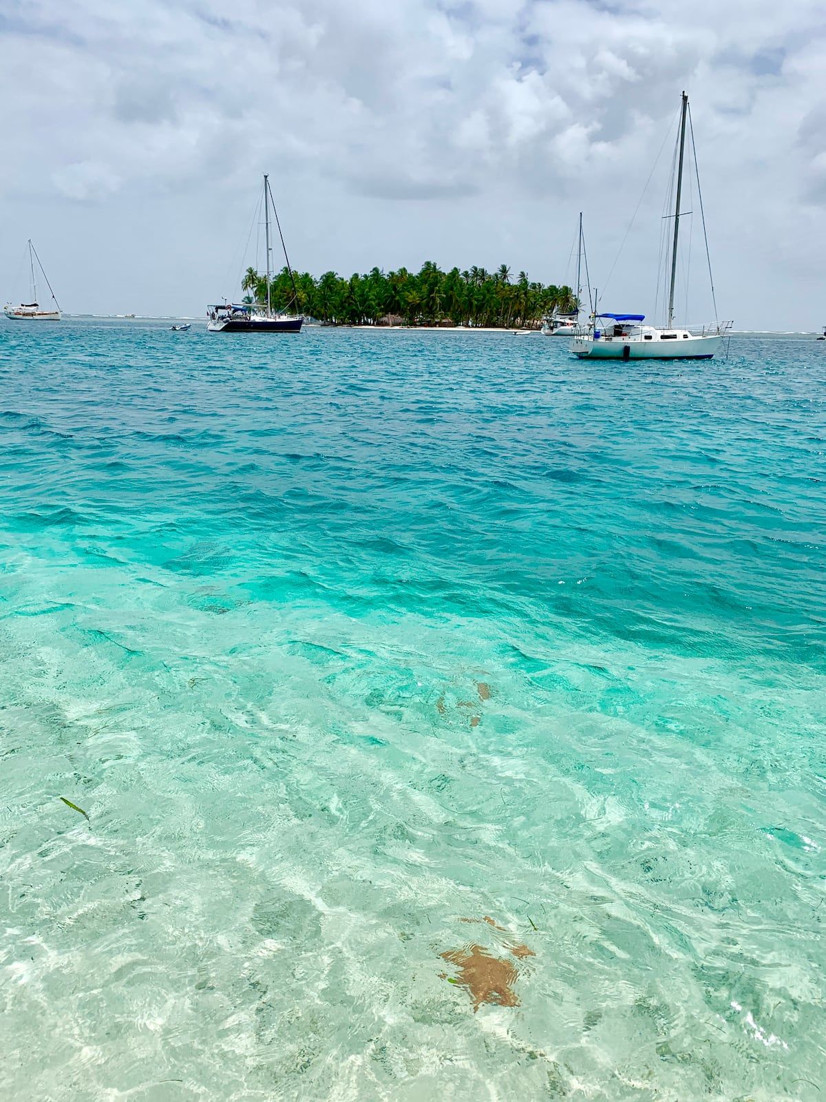 Crystal-clear turquoise waters and sailboats near a tropical island in the San Blas Islands, Panama. Perfect for a day trip adventure.