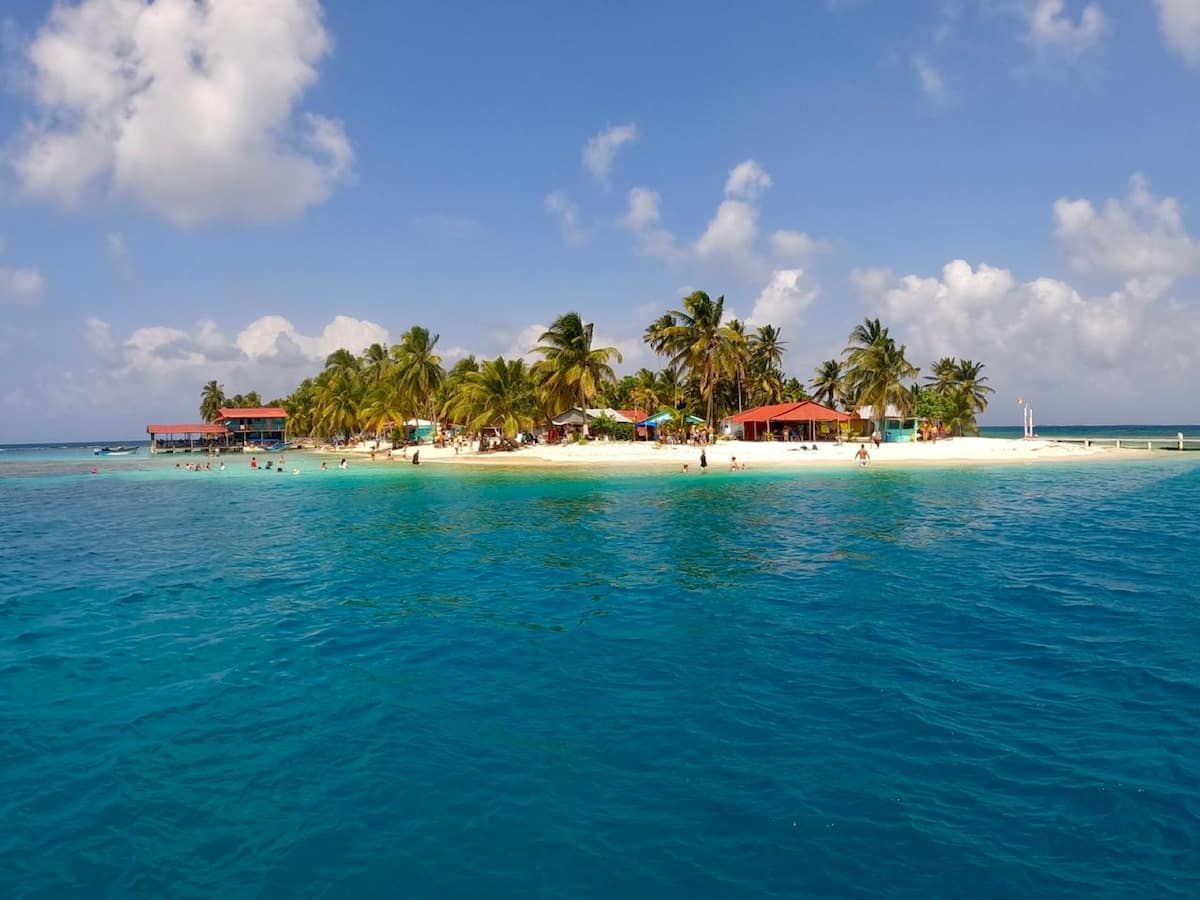 Vibrant tropical beach in the San Blas Islands, Panama, with turquoise waters, palm trees, and colorful huts under a sunny sky.