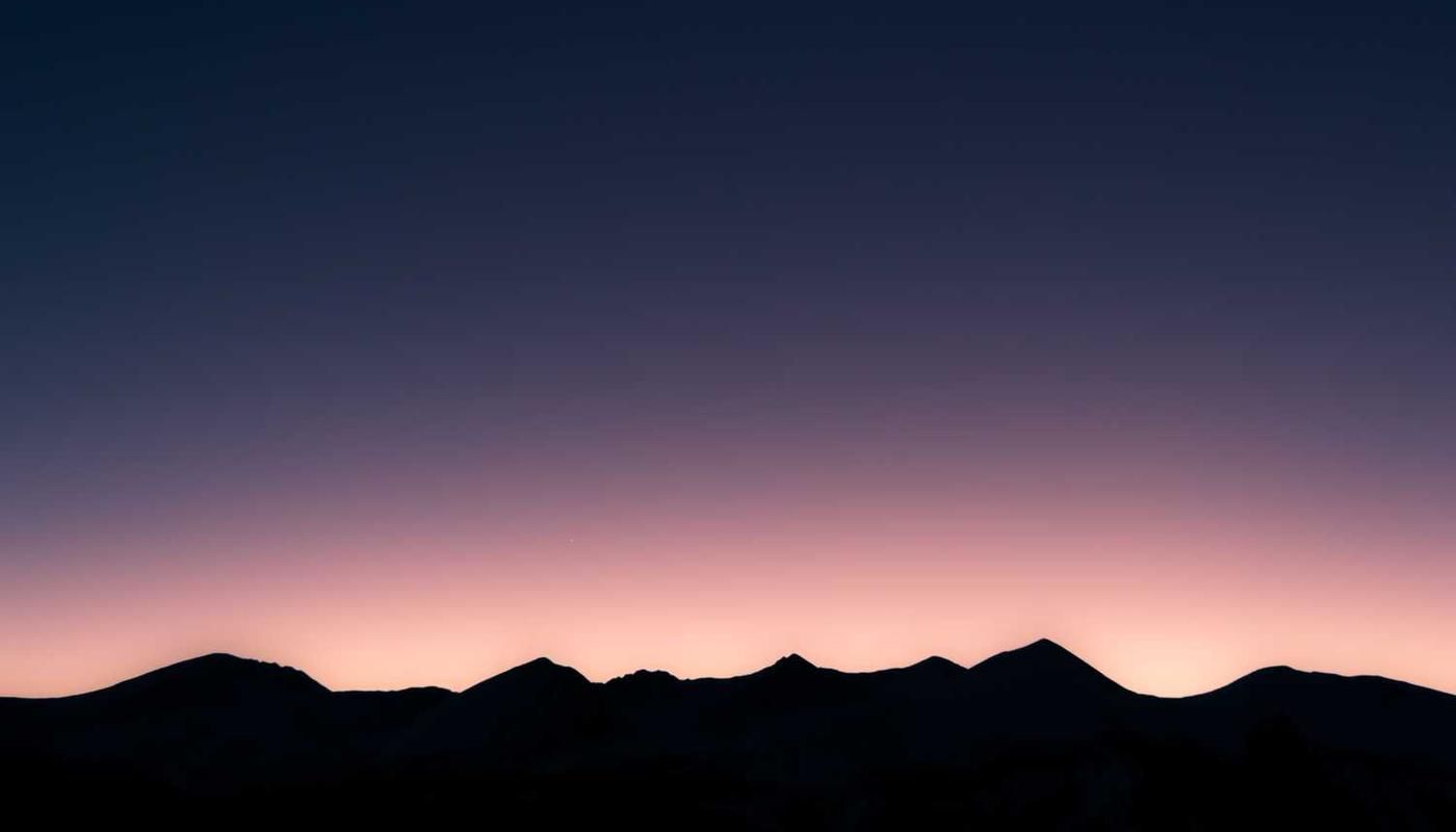 Silhouetted mountain range at dusk with a gradient sky transitioning from deep blue to soft pink, capturing the tranquil beauty of Panama City's natural backdrop.