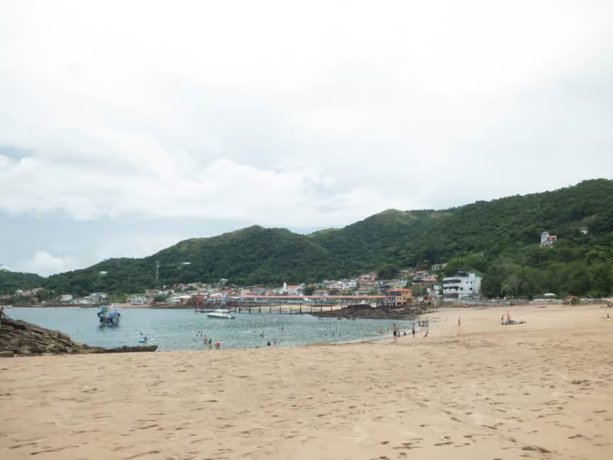 Golden sandy beach at Taboga Island with turquoise waters, lush green mountains, and a small coastal village under a cloudy sky.