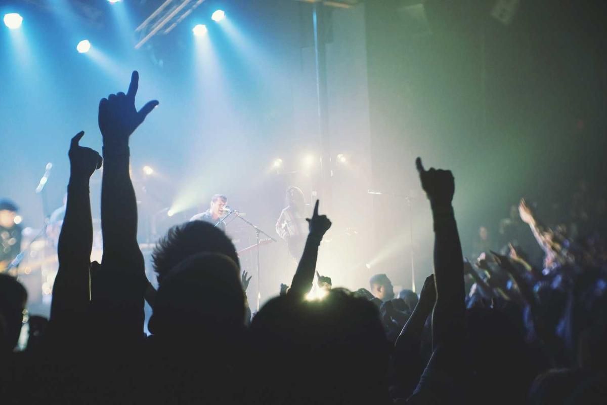 Crowd at a concert with hands raised in the air, illuminated by blue stage lights, capturing the energy of a live music event.