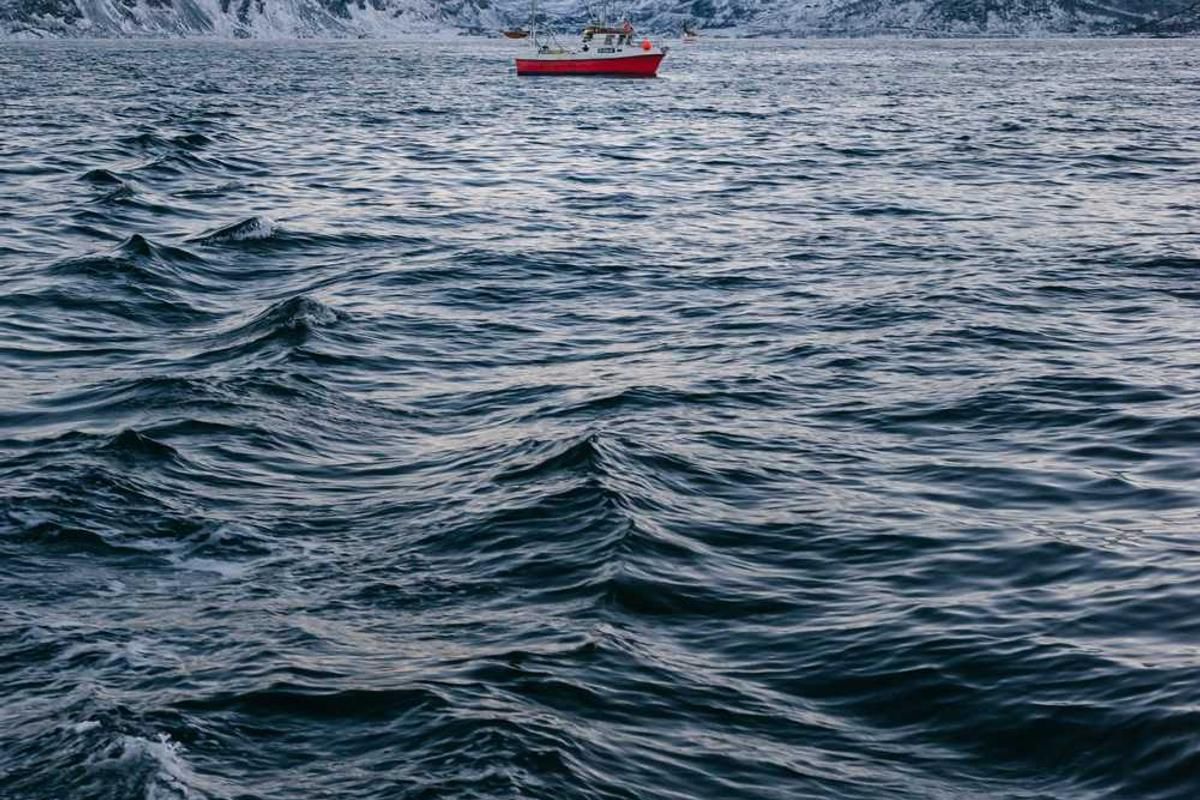 A red and white boat sails on calm waters near snow-capped mountains during dawn or dusk.