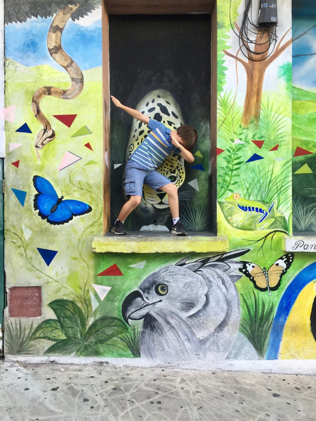 Child posing in front of a colorful jungle mural featuring a jaguar, anaconda, butterflies, and tropical foliage during a rooftop dining tour in Panama City.