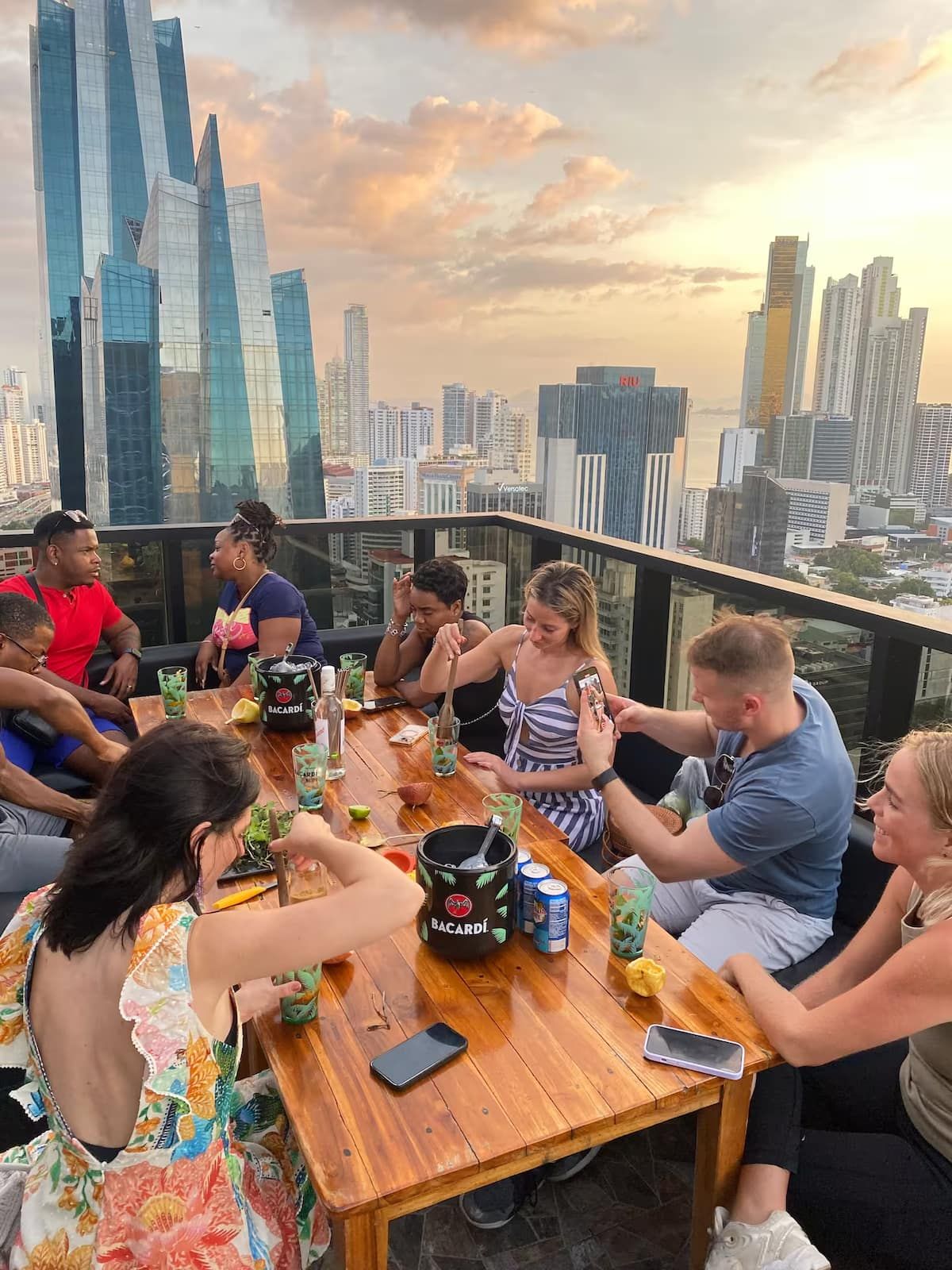 Group of friends enjoying local bites and cocktails on a rooftop bar in Panama City during sunset, with a stunning view of the city skyline.