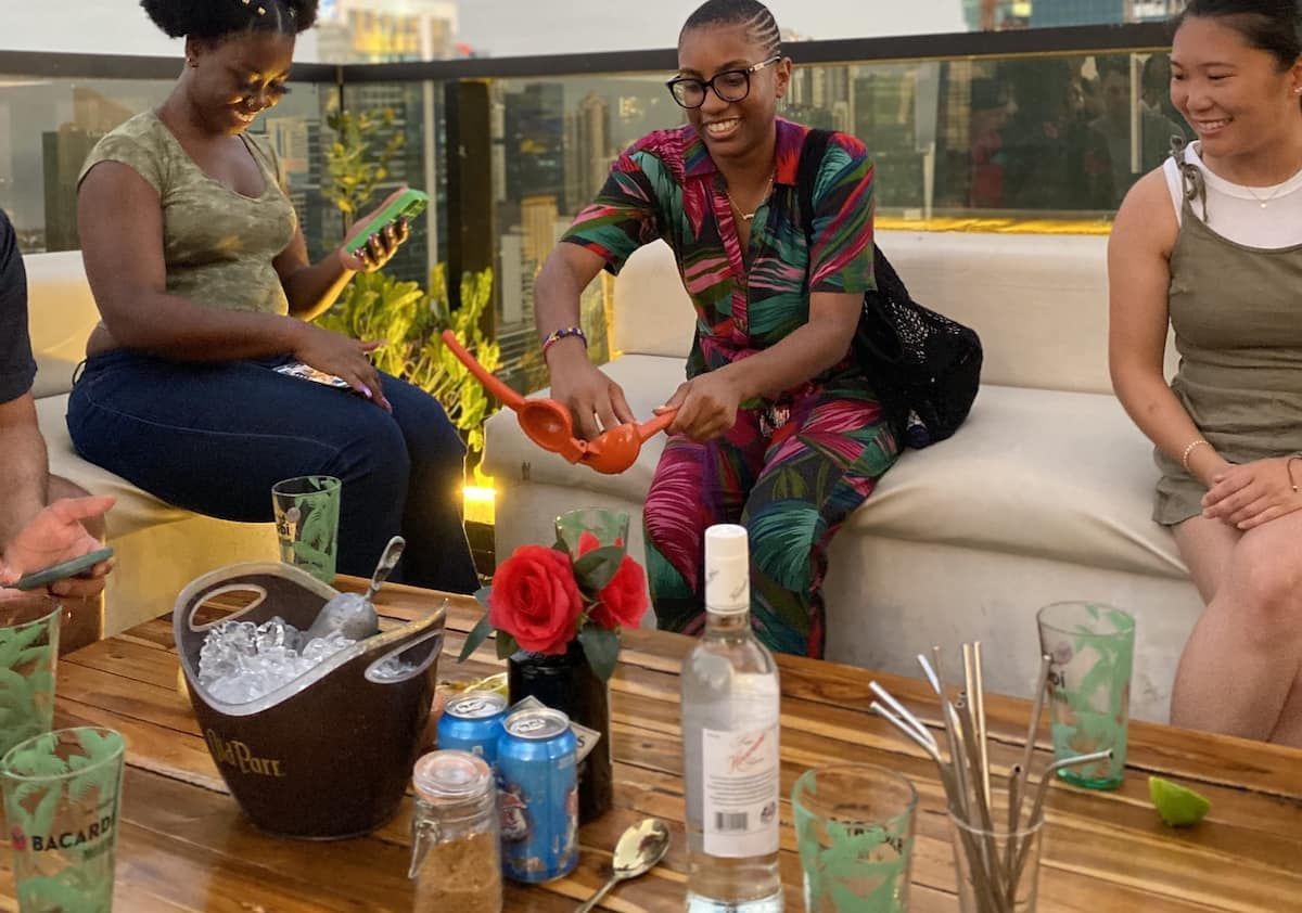 Friends enjoying local bites and drinks on a rooftop bar in Panama City at sunset, with one person squeezing a lime into a cocktail.