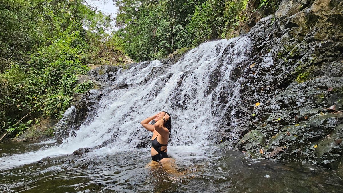 A woman in a black swimsuit enjoying a refreshing dip under a cascading waterfall surrounded by lush greenery in Panama City, Panama.