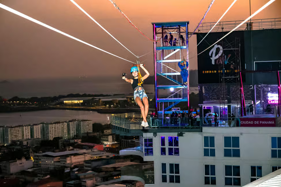 A woman ziplines over the Panama City skyline at night, offering a thrilling urban adventure with stunning city views.