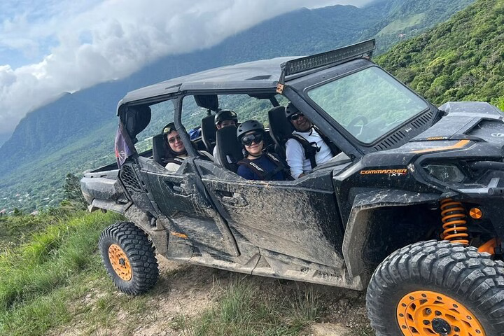 Group of adventurers riding a muddy ATV through a lush jungle landscape in Panama City, surrounded by towering green hills and cloudy skies.